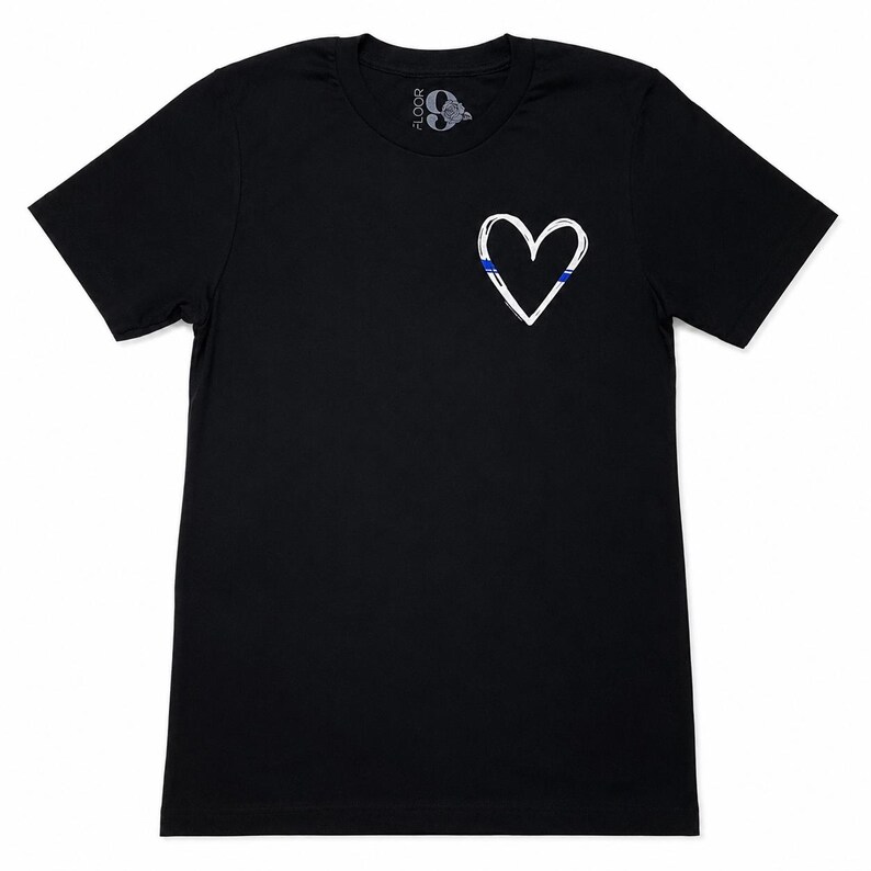 May include: A black short-sleeved t-shirt featuring a white hand-drawn heart outline on the left chest. The heart design includes a thin horizontal blue stripe accent. The inner neck label displays the text FLOOR 9 with a rose graphic.