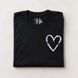 May include: A black short-sleeved t-shirt featuring a white hand-drawn heart outline on the front right side. The heart includes a thin horizontal blue stripe. The inner neck label displays the text FLOOR 9 with a rose graphic illustration.
