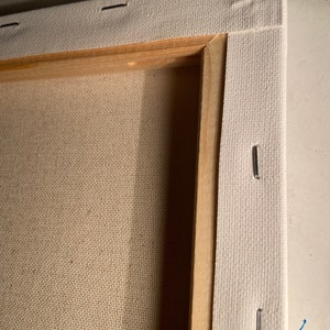 May include: Close-up of the edge of a stretched canvas, showing the wooden frame and staples securing the canvas to the frame.