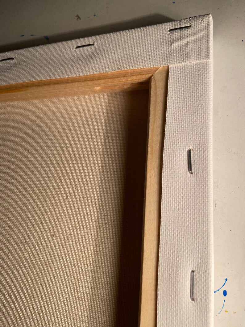 May include: Close-up of the edge of a stretched canvas, showing the wooden frame and staples securing the canvas to the frame.