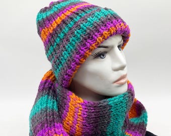 May include: A knitted hat and scarf set in a vibrant color palette of teal, purple, orange, and gray stripes. The hat is a close-fitting beanie style, and the scarf is long and rectangular. The set is displayed on a mannequin head.