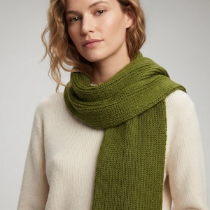May include: A chunky knit scarf in a solid olive green color featuring a ribbed texture. The scarf is wrapped around the neck and hangs down in a straight, vertical line, showcasing a thick, consistent yarn construction and a simple, classic design.