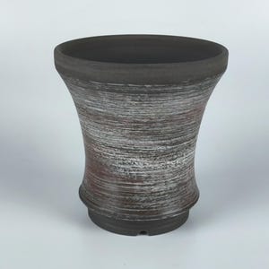 Peut inclure: Un pot en céramique brun foncé et blanc avec une large ouverture évasée et une base étroite. Le pot a un design texturé et rayé.