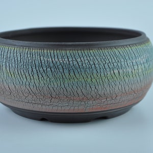 May include: A round, brown ceramic pot with a crackled glaze in shades of blue, green, and red. The pot has a wide opening and a slightly rounded bottom.