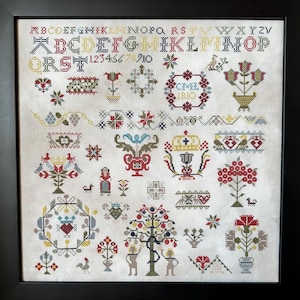 Könnte beinhalten: Ein gerahmter Kreuzstich-Sampler mit weißem Hintergrund und bunter Stickerei. Der Sampler zeigt ein Alphabet, Zahlen und verschiedene florale und geometrische Muster. Der Text "CMEL 1810" ist in der oberen rechten Ecke gestickt.