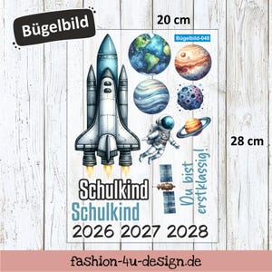 Könnte beinhalten: Ein Bügelbild mit Weltraum-Motiven, darunter eine Rakete, Planeten, ein Astronaut und der Text "Schulkind" und "Du bist erstklassig!" Das Bügelbild misst 20 cm x 28 cm.