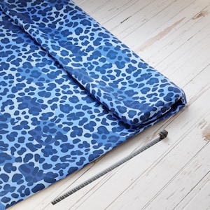 Könnte beinhalten: Blauer und weißer Leopardenmusterstoff. Der Stoff ist gefaltet und ein Maßband liegt auf einer weißen Holzoberfläche.