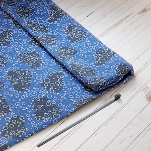 Könnte beinhalten: Blauer Stoff mit einem Muster aus weißen und grauen Kreisen und wolkenartigen Formen. Der Stoff ist gefaltet und zeigt die Unterseite. Ein schwarzes Maßband befindet sich auf der rechten Seite des Stoffes.
