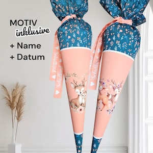 Könnte beinhalten: Zwei pfirsichfarbene Schultüten mit Hirschillustrationen und tealfarbenen floralen Oberteilen. Die Tüten haben ein weißes Band und ein Band mit Text. Der Text "MOTIV inklusive + Name + Datum" ist sichtbar.