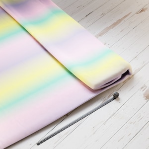 Könnte beinhalten: Ein gefaltetes Stück Stoff mit einem Regenbogen-Ombre-Muster. Der Stoff ist in der Mitte gefaltet und die Kanten sind sichtbar. Der Stoff liegt auf einer weißen Holzoberfläche.