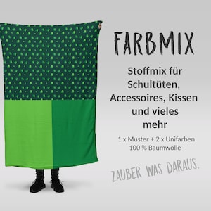 Könnte beinhalten: Ein grün-weiß gemusterter Stoff mit dem Text "FARBMIX" und anderem deutschen Text. Der Stoff ist in Abschnitte in verschiedenen Grüntönen unterteilt. Der Text lautet "100% Baumwolle".