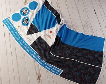 May include: A white and blue fabric with the text "SCHULKIND" printed on a blue border. The fabric features blue circles with star designs and a blue and black patterned section with red accents.