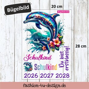 Könnte beinhalten: Ein Bügelbild mit einem bunten Delfin, der aus Wellen springt, umgeben von tropischen Blumen. Das Design enthält den Text "Schulkind" und die Jahreszahlen 2026, 2027 und 2028. Das Bügelbild misst ca. 20 cm breit und 28 cm hoch.