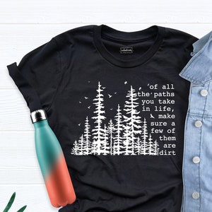May include: Black t-shirt with a white graphic of a forest and the text 'of all the paths you take in life, make sure a few of them are dirt'.