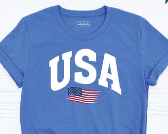 May include: Blue t-shirt with the word "USA" in white block letters and a small American flag graphic. The shirt has rolled-up sleeves and a knotted hem. The brand "coolandtrendy design" is printed in the lower right corner.