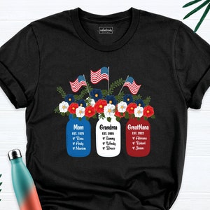 K&ouml;nnte beinhalten: Schwarzes T-Shirt mit einem Design aus drei Einmachgl&auml;sern mit roten, wei&szlig;en und blauen Blumen und amerikanischen Flaggen. Die Gl&auml;ser sind mit "Mutter", "Oma" und "Urgro&szlig;mutter" sowie Namen und Daten beschriftet.