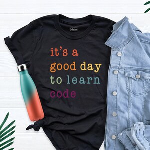 May include: Black t-shirt with the text "it's a good day to learn code" in rainbow colors.