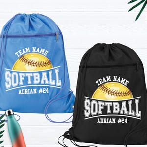 May include: Two drawstring bags with a softball design. The bag on the left is blue with a white softball and the text "TEAM NAME SOFTBALL ADRIAN #24". The bag on the right is black with a white softball and the text "TEAM NAME SOFTBALL ADRIAN #24".