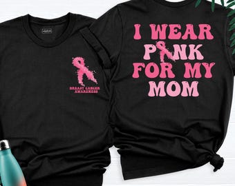 May include: A black t-shirt featuring a pink breast cancer awareness ribbon on the front left chest with the text Breast Cancer Awareness. The back displays the text I Wear Pink For My Mom in large pink letters with a pink ribbon replacing the letter I.