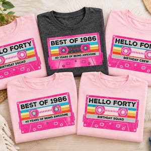 Pu&ograve; includere: Cinque magliette a maniche corte in rosa chiaro e grigio scuro. Ogni maglietta presenta la grafica di una cassetta audio retr&ograve; con strisce colorate. Il testo recita HELLO FORTY, BIRTHDAY SQUAD, BEST OF 1986 e 40 YEARS OF BEING AWESOME.