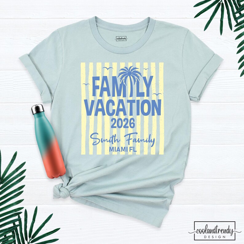 May include: A light blue t-shirt featuring a graphic with yellow vertical stripes, a blue palm tree, and the text "FAMILY VACATION 2026 Smith Family MIAMI FL". Beside the shirt is a teal and orange gradient metal water bottle.