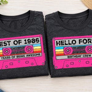 Pu&ograve; includere: Due magliette grigio scuro a girocollo con una grafica a cassetta retr&ograve;. La maglietta a sinistra riporta il testo BEST OF 1986 e 40 YEARS OF BEING AWESOME. La maglietta a destra riporta il testo HELLO FORTY e BIRTHDAY CREW in rosa, giallo e blu.