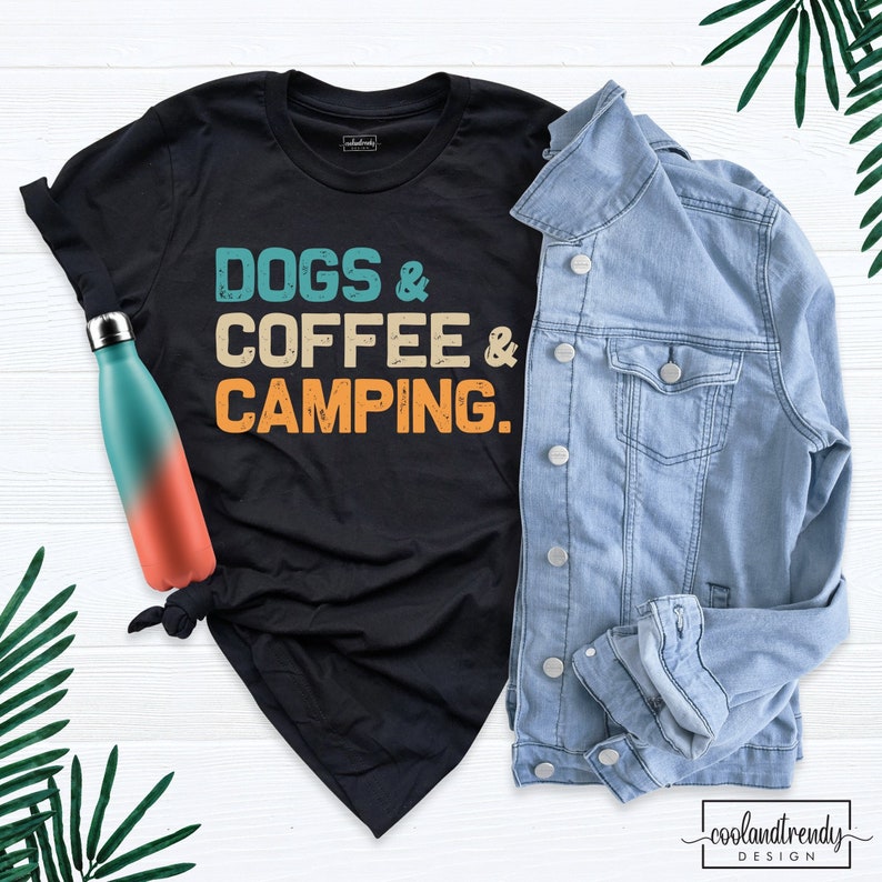Pu&ograve; includere: Maglietta nera con il testo "Dogs & Coffee & Camping." in un font di stile vintage. Il testo &egrave; in tonalit&agrave; di blu, arancione e giallo.