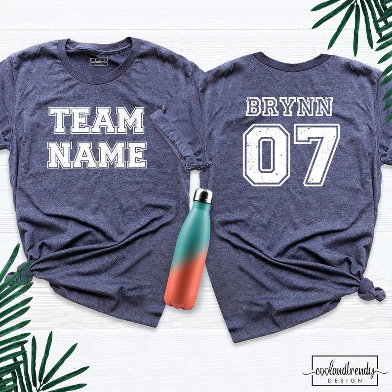 Puede incluir: Dos camisetas azul marino con letras blancas. Una camiseta dice "TEAM NAME" y la otra "BRYNN 07". Una botella de agua con degradado turquesa y naranja est&aacute; en el centro. Las camisetas son probablemente para un equipo deportivo.
