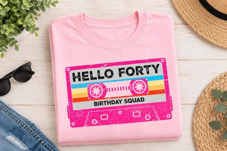 Pu&ograve; includere: Una t-shirt rosa chiaro con la grafica di una cassetta audio retr&ograve; nei toni del rosa, giallo e blu. Il testo "HELLO FORTY" &egrave; stampato in nero sopra la cassetta, e "BIRTHDAY SQUAD" &egrave; stampato in nero sotto la grafica della cassetta.
