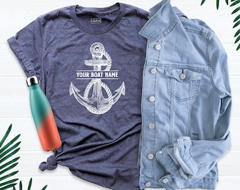May include: A heather navy blue t-shirt featuring a white graphic of an anchor wrapped in rope with the text YOUR BOAT NAME, paired with a light blue denim jacket and a teal and coral gradient metal water bottle.