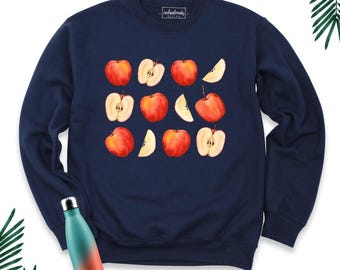 May include: A navy blue crewneck sweatshirt featuring a repeating pattern of red apples and apple slices across the chest. The interior neck label displays the text "coolandtrendy DESIGN". A gradient teal and orange water bottle is positioned below.