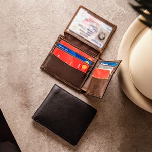 May include: A black leather wallet and a brown leather wallet, both open to show credit cards and a driving licence. The brown wallet is open, revealing multiple card slots. The black wallet is closed.