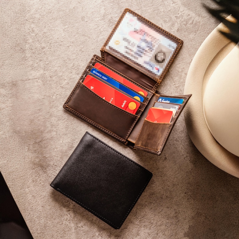 May include: A black leather wallet and a brown leather wallet, both open to show credit cards and a driving licence. The brown wallet is open, revealing multiple card slots. The black wallet is closed.
