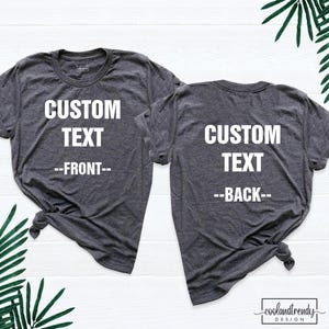 May include: Two dark charcoal gray short-sleeve t-shirts with white text. The left shirt displays CUSTOM TEXT --FRONT-- and the right shirt displays CUSTOM TEXT --BACK--. Both shirts feature a crew neckline and a knotted hem detail on the side.