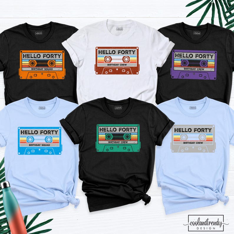 Pu&ograve; includere: Sei magliette a maniche corte nere, bianche e azzurre, ognuna con una grafica a cassetta retr&ograve;. I disegni includono il testo "HELLO FORTY" e "BIRTHDAY SQUAD" o "BIRTHDAY CREW" in arancione, rosso, viola, blu, verde o grigio.