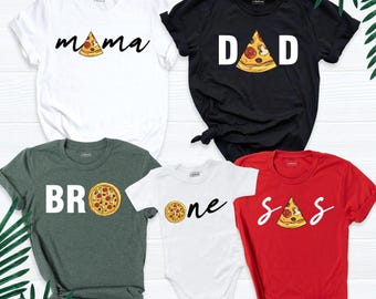 May include: A collection of five shirts and a bodysuit featuring pizza-themed graphics. The white shirt says mama, the black shirt says dad, the dark green shirt says bro, the white bodysuit says one, and the red shirt says sis.