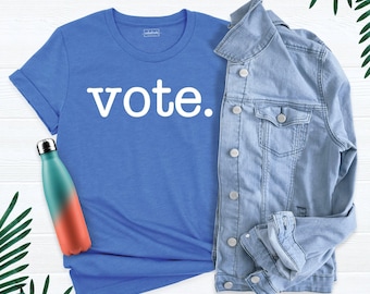 May include: A blue short-sleeved t-shirt with the word vote. printed in white letters on the front, paired with a light blue denim jacket and a teal and orange gradient metal water bottle with a silver cap.