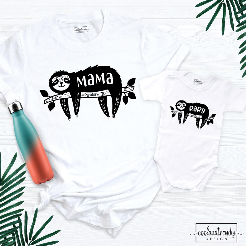 May include: White t-shirt with a black sloth design and the word "mama". A matching white baby onesie features a similar sloth design with the word "baby". A teal and orange water bottle is visible on the left.