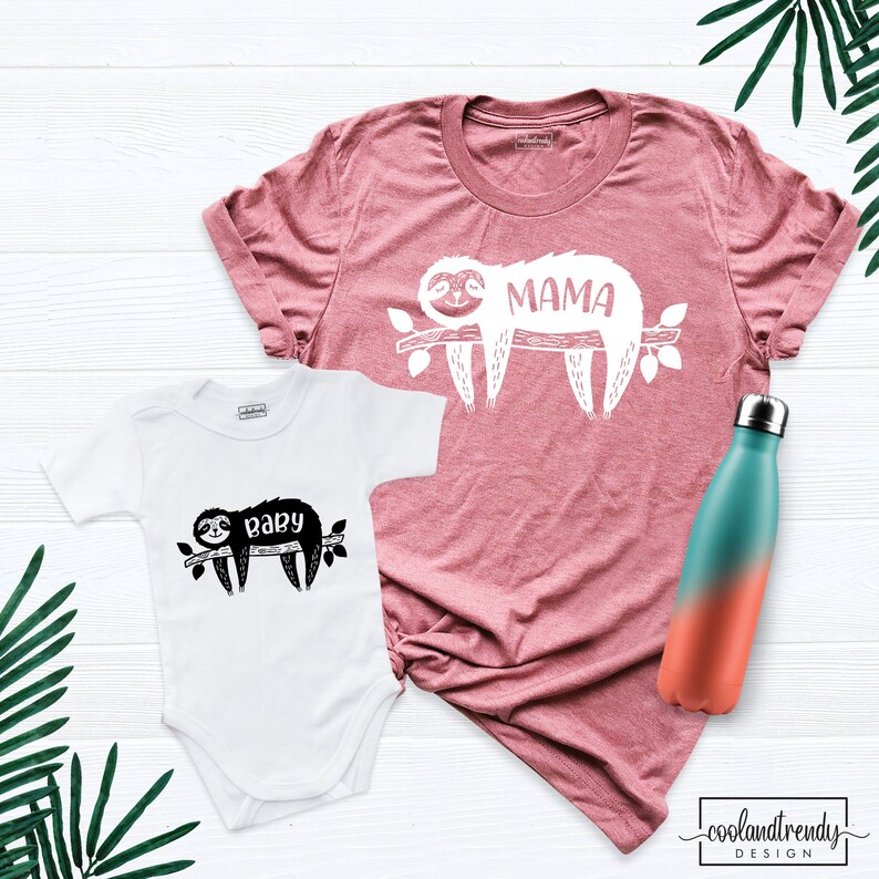 May include: A white baby onesie with a black sloth graphic and the word "baby". A dusty rose t-shirt with a white sloth graphic and the word "MAMA". A teal and orange ombre water bottle.