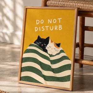 May include: A rectangular framed wall art print featuring a mustard yellow background with the white text DO NOT DISTURB. Two cats, one black and one calico, are tucked under a green and white striped blanket with their eyes closed.