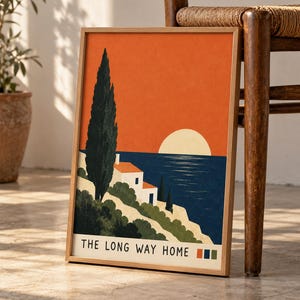 May include: A framed art print featuring a coastal landscape with a tall dark green cypress tree, a white house with a red roof, and a large pale yellow sun against a deep orange sky. The text THE LONG WAY HOME is printed at the bottom.