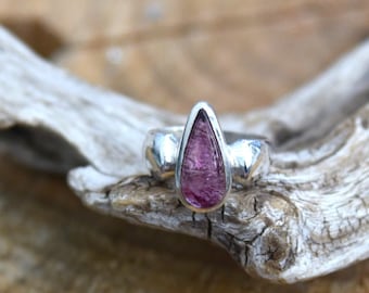May include: A silver ring with a teardrop-shaped pink gemstone set in the center.