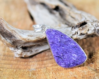 May include: A purple and silver pendant featuring a large, iridescent, teardrop-shaped stone. The pendant is resting on a piece of driftwood.