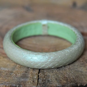 May include: A silver bangle bracelet with a green interior. The bracelet has a textured surface.