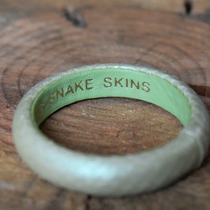 Pu&ograve; includere: Un braccialetto in pelle bianca con interno verde e le parole "SNAKE SKINS" incise in oro.