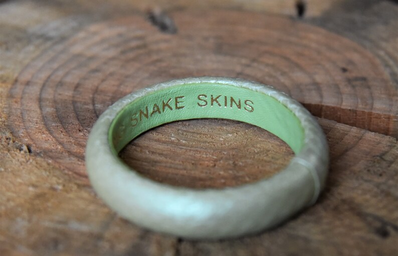 Pu&ograve; includere: Un braccialetto in pelle bianca con interno verde e le parole "SNAKE SKINS" incise in oro.