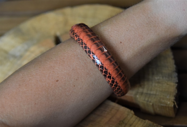 Puede incluir: Un brazalete de piel de serpiente de color naranja brillante y negro en una mu&ntilde;eca.