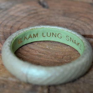 Pu&ograve; includere: Un braccialetto in pelle verde chiaro con il testo "KAM LUNG SNAKE" inciso in lettere dorate.