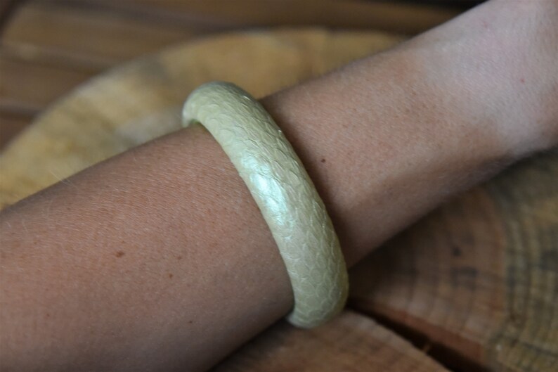 Pu&ograve; includere: Un braccialetto bianco a forma di bangle con una superficie testurizzata. Il braccialetto &egrave; realizzato in un materiale liscio e lucido.