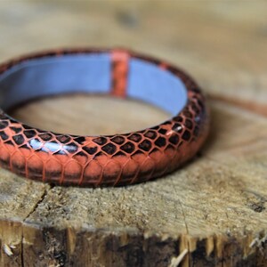 Puede incluir: Un brazalete ancho de color naranja y negro con un patr&oacute;n de piel de serpiente.